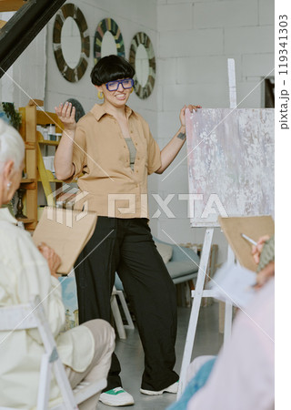Vertical shot of young fashionable teacher giving drawing lesson in modern white studio 119341303