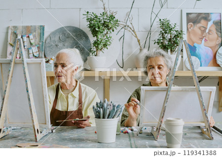 Two senior best friends painting on canvas together during art therapy Two senior best friends painting on canvas together during art therapy 119341388