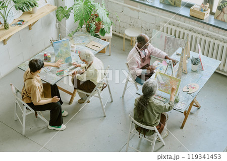 High angle shot of retro drawing studio with biracial people of different age sitting at work desks and painting on canvas High angle shot of retro drawing studio with biracial people of different age sitting at work desks and painting on canvas 119341453