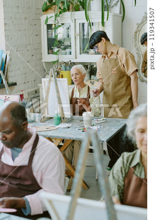 Vertical shot of young adult drawing teacher checking her senior student who trying to study new drawing technique in background 119341507