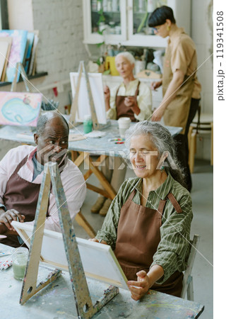 Vertical high angle shot of African American husband looking at his Caucasian wife with love while she painting on canvas Vertical high angle shot of African American husband looking at his Caucasian wife with love while she painting on canvas 119341508