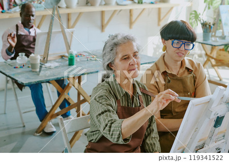 High angle shot of group of senior people drawing with oils paints on canvas while their young female teacher watching them High angle shot of group of senior people drawing with oils paints on canvas while their young female teacher watching them 119341522