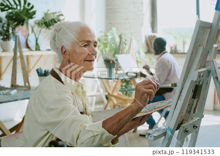 Medium close up of senior refined woman painting on canvas in drawing studio during her art therapy attendance Medium close up of senior refined woman painting on canvas in drawing studio during her art therapy attendance 119341533
