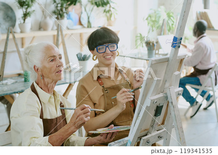 High angle shot of senior elegant student holding paintbrush and palette admiring sketch on canvas with her young drawing teacher 119341535
