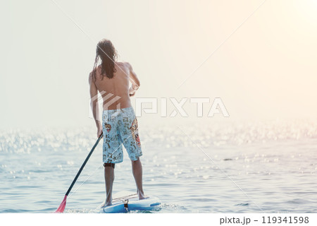 Man Paddleboarding Ocean Sunset - A man is paddleboarding on a calm ocean at sunset. Man Paddleboarding Ocean Sunset - A man is paddleboarding on a calm ocean at sunset. 119341598