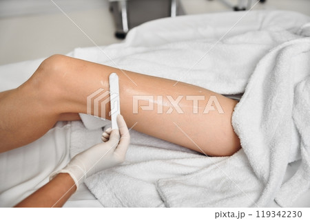 Waxing treatment on a clients leg in a clean salon setting in daylight Waxing treatment on a clients leg in a clean salon setting in daylight 119342230