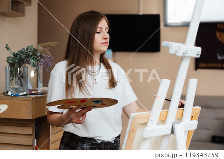 Young artist painting on canvas with palette in a bright studio 119343259