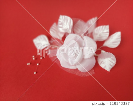 A stunning white rose stands out beautifully against a rich red background, complemented by soft leaves and small pearl accents, ideal for a wedding setting 119343387