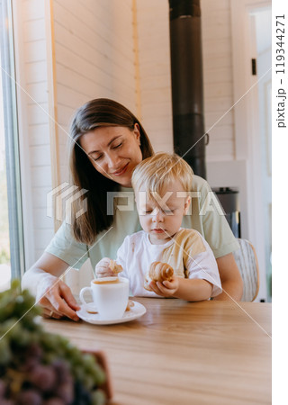 Mother and child enjoying breakfast with coffee and croissants in kitchen, sharing a peaceful moment 119344271