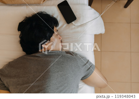 Close up face of sleepy man slept with his mobile phone left near his head. Close up face of sleepy man slept with his mobile phone left near his head. 119348043