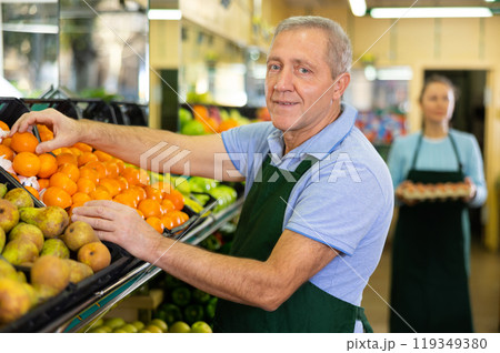 Skillful elderly salesman laying out tangerines in shop Skillful elderly salesman laying out tangerines in shop 119349380