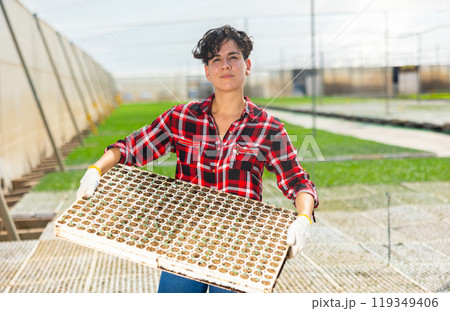 Organic food production concept. Portrait of young woman holding nursery trays at vegetable cultivation farm Organic food production concept. Portrait of young woman holding nursery trays at vegetable cultivation farm 119349406