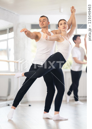 Happy young caucasian man and woman practicing ballet arabesque pose in ballroom Happy young caucasian man and woman practicing ballet arabesque pose in ballroom 119349463