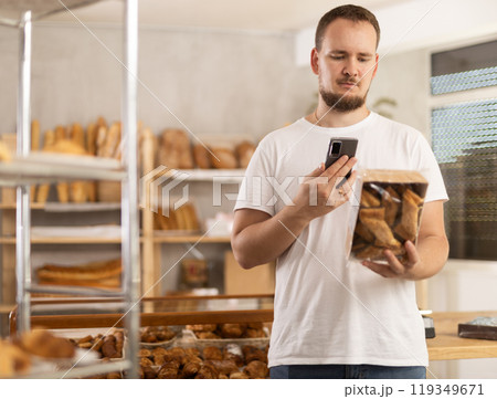 Man customer at bakery scans QR code on cookie package using phone camera Man customer at bakery scans QR code on cookie package using phone camera 119349671