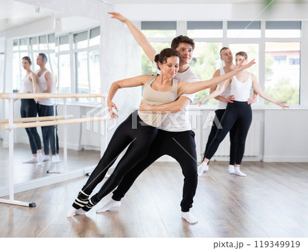 Positive duet of gymnasts rehearsing performance with support, modern ballet dancers in pair during group training session in ballet hall Positive duet of gymnasts rehearsing performance with support, modern ballet dancers in pair during group training session in ballet hall 119349919