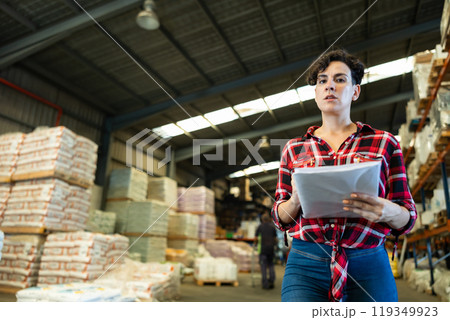 Female storekeeper checks presence of goods in the building materials warehouse Female storekeeper checks presence of goods in the building materials warehouse 119349923