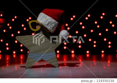 Wooden star with Santa's hat on dark bokeh light garland background. New year and Christmas preparation. Handmade eco-friendly decor. Sustainable Christmas decoration 119350138