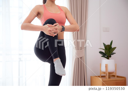 Beautiful young asian woman standing workout with warmup and stretch muscle leg at home. 119350530