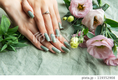 Elegant green manicure displayed alongside fresh pink and white flowers on a soft fabric  119352908