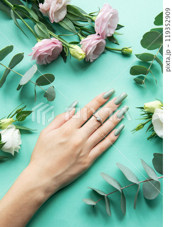 Elegant hand with manicured nails surrounded by fresh flowers and greenery on a turquoise background Elegant hand with manicured nails surrounded by fresh flowers and greenery on a turquoise background 119352909