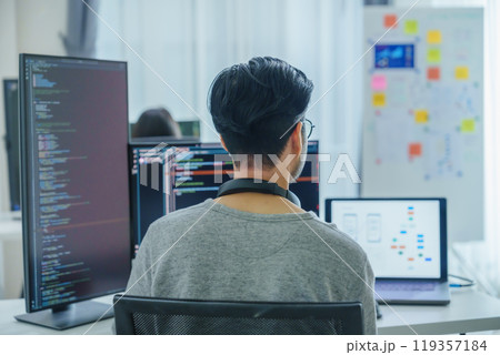 Asian software developers working on multiple screens displaying code and application diagrams in a modern office 119357184