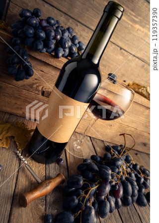 Bottle of red wine and blue grapes on a old wooden table. 119357390