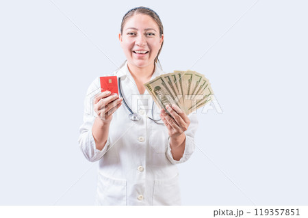 Happy female doctor holding credit card and money isolated. Smiling young female doctor holding money and credit cards 119357851
