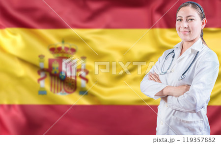 Spanish Health and Care concept. Portrait of female doctor on Spain flag. Doctor with arms crossed on Spanish flag Spanish Health and Care concept. Portrait of female doctor on Spain flag. Doctor with arms crossed on Spanish flag 119357882
