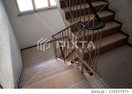 A simple indoor apartment building staircase with a tiled floor and natural light streaming through a window, creating a serene and minimalist atmosphere. 119357973