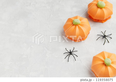 Three orange pumpkin shaped treats with green tops, accompanied by small black spider decorations Three orange pumpkin shaped treats with green tops, accompanied by small black spider decorations 119358075