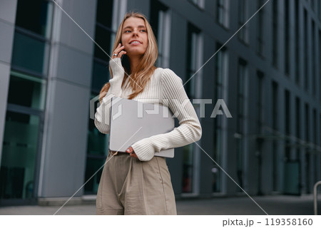 A young professional woman talks on her phone outdoors, enjoying a casual chic city vibe 119358160