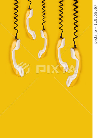 A few yellow old phone handsets dangle on wire. yellow background vertical banner poster copy space A few yellow old phone handsets dangle on wire. yellow background vertical banner poster copy space 119358667
