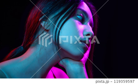 Portrait of beautiful young Korean girl posing against black background with blue and pink neon lights Portrait of beautiful young Korean girl posing against black background with blue and pink neon lights 119359597