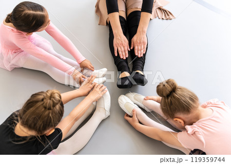Little girls with teacher stretching legs together in ballet class Little girls with teacher stretching legs together in ballet class 119359744