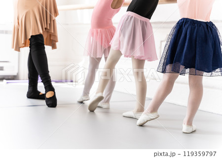 Little girls standing gracefully in tutus learning classical dance from her teacher at barre 119359797
