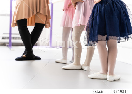 Little girls standing gracefully in tutus learning classical dance from her teacher at barre 119359813