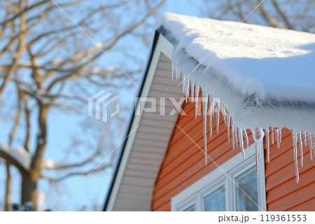 Icicles hang from a snow covered roof of an orange house on a bright, sunny winter day 119361553