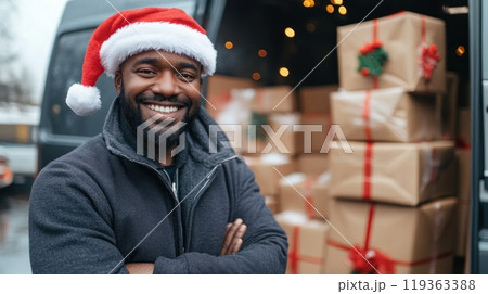 Smiling African American delivery man wearing Santa hat stands in front of his van 119363388