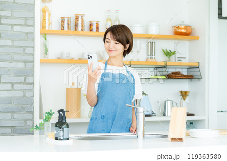 キッチンでスマホを持つ笑顔の女性 キッチンでスマホを持つ笑顔の女性 119363580