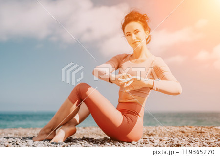 Middle aged well looking woman with black hair, fitness instructor in leggings and tops doing stretching and pilates on yoga mat near the sea. Female fitness yoga routine concept. Healthy lifestyle Middle aged well looking woman with black hair, fitness instructor in leggings and tops doing stretching and pilates on yoga mat near the sea. Female fitness yoga routine concept. Healthy lifestyle 119365270