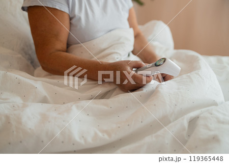 Illness tired Caucasian 50s senior woman touching forehead after using thermometer to checking body temperature and take medicine lying under blanket on bed. Sick female with cold lying in bed with Illness tired Caucasian 50s senior woman touching forehead after using thermometer to checking body temperature and take medicine lying under blanket on bed. Sick female with cold lying in bed with 119365448