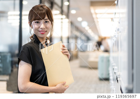 郵便受けの前で定形外郵便封筒を抱える女性 郵便受けの前で定形外郵便封筒を抱える女性 119365697