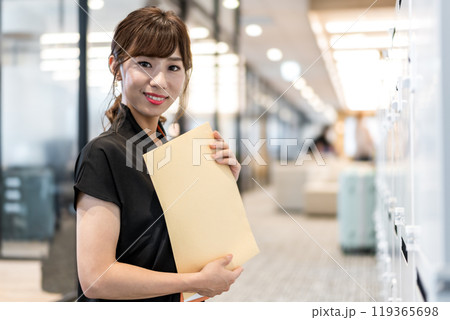 郵便受けの前で定形外郵便封筒を抱える女性 119365698