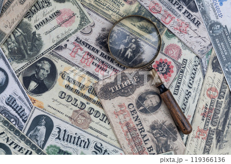 Old US banknotes and silver certificates with silver dollar coins and magnifying glass 119366136