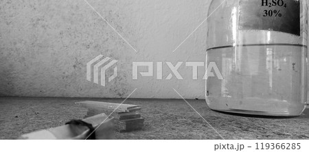 Glass Bottle with Sulfuric Acid Solution Against a Textured Wall 119366285
