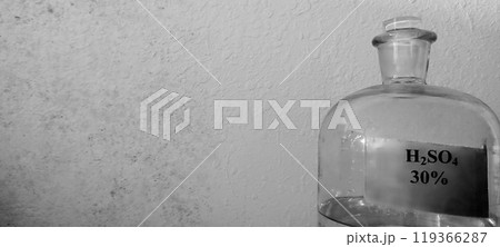 Glass Bottle with Sulfuric Acid Solution Against a Textured Wall 119366287