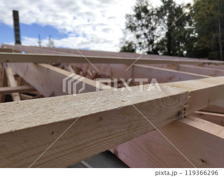 Wooden beams in the early stages of construction, against a backdrop of cloudy sky and trees, capturing the rugged texture of fresh lumber 119366296