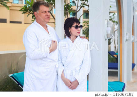 Adult couple in white robes relaxing near the pool 119367195