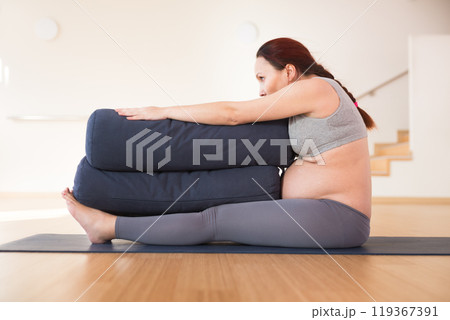 Pregnant woman is engaged in yoga. Seated Forward Fold or Paschimottanasana Pregnant woman is engaged in yoga. Seated Forward Fold or Paschimottanasana 119367391