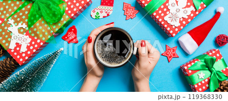 Top view of woman holding a cup of coffee in her hands on blue background. Christmas decorations. New year time concept 119368330